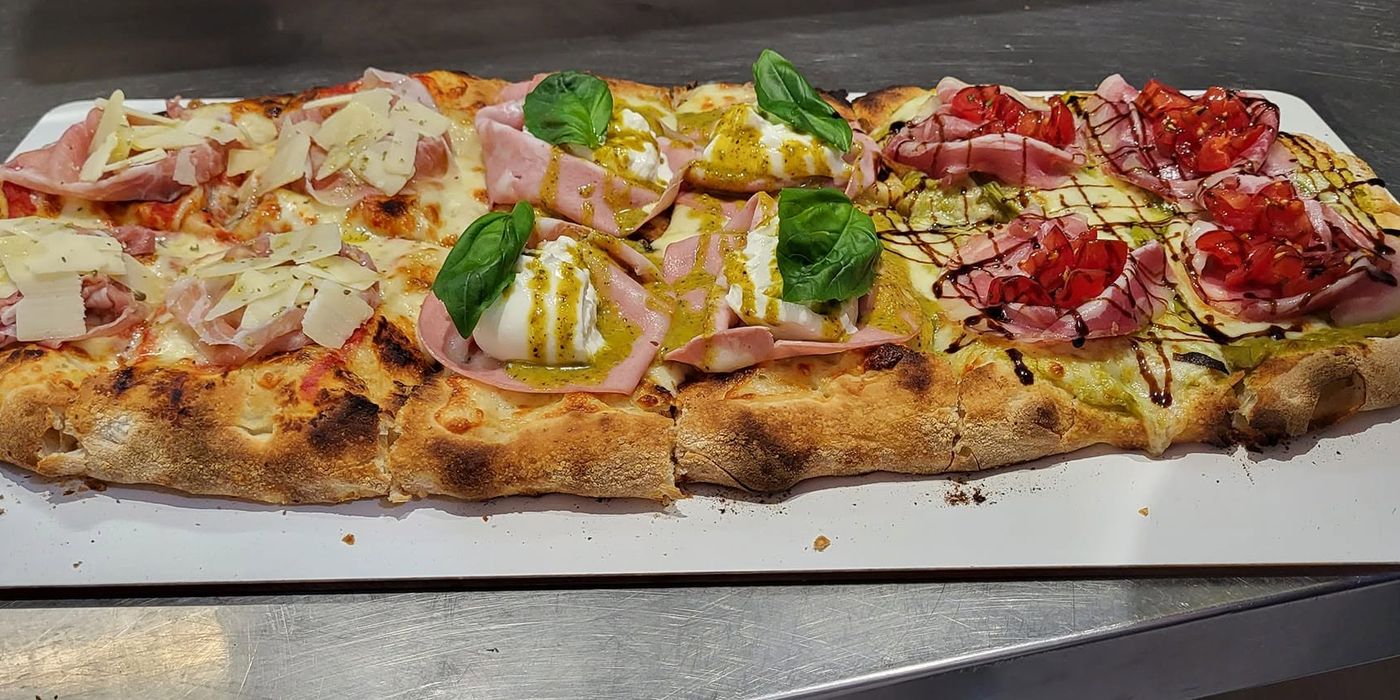 Una pizza in pala divisa in tre gusti: crudo e scaglie di grana, mortadella e burrata, pomodorini e glassa balsamica
